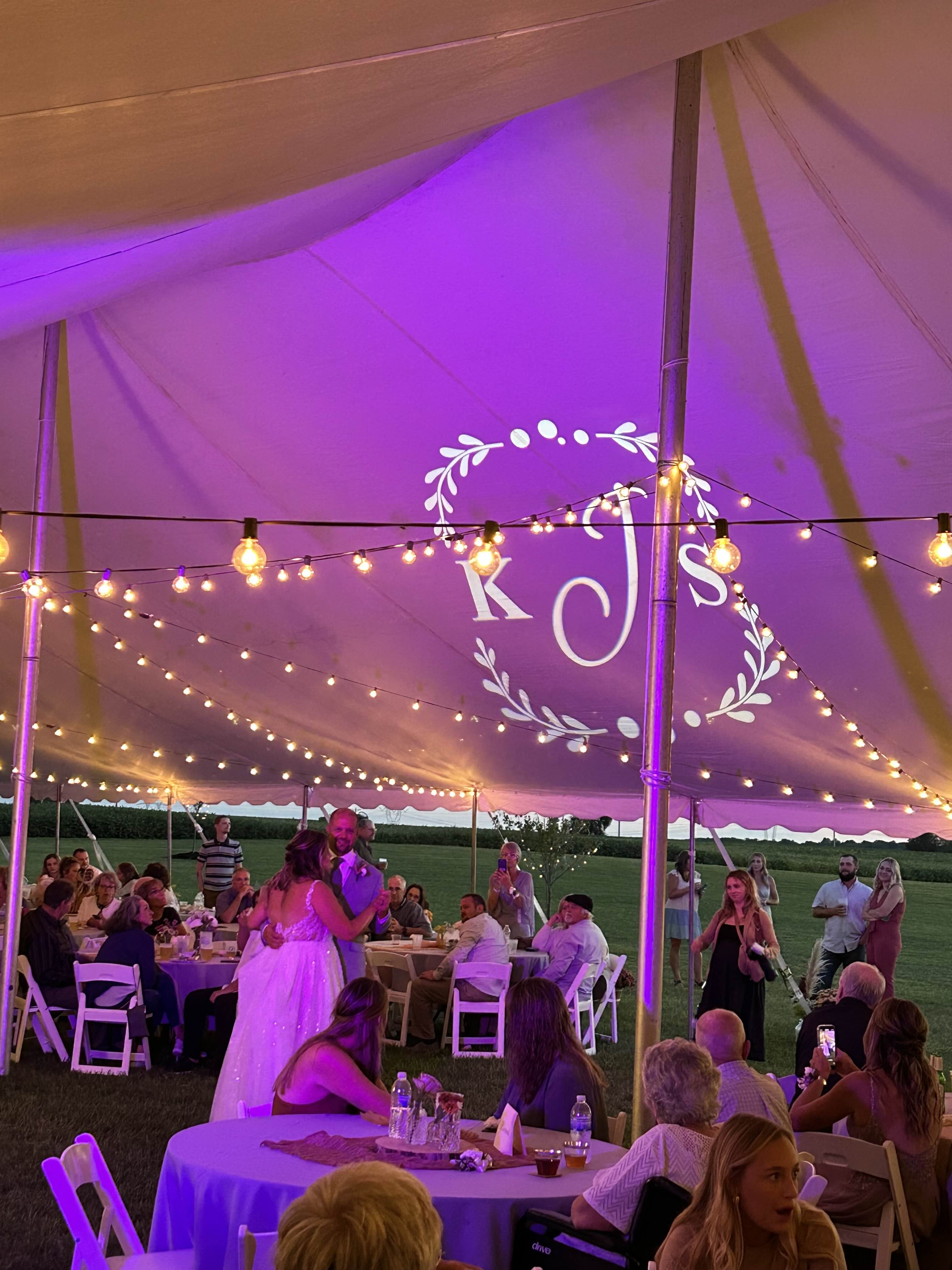 Outdoor wedding reception under tent with purple uplighting and string lights